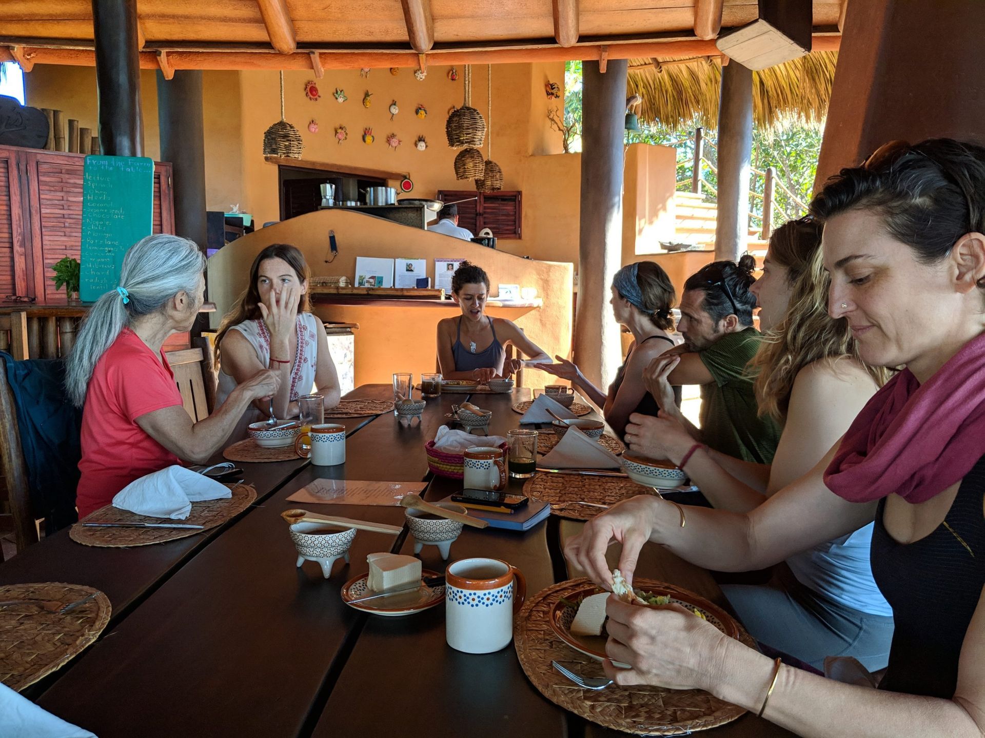 People sitting around a long table sharing a meal in a rustic open-air dining area
