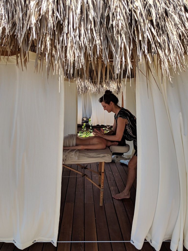 Person seated at a table under a thatched canopy, preparing food beside white curtains.