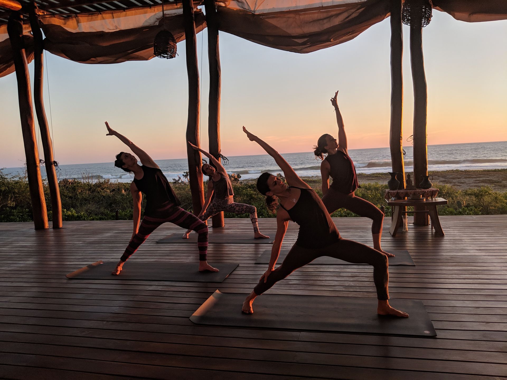 People doing yoga poses on a wooden deck at sunset overlooking the ocean