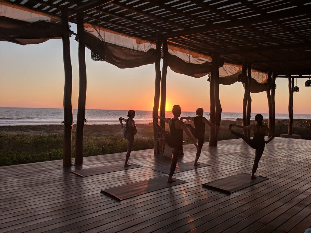 People exercising on yoga mats in an open pavilion at sunset by the ocean