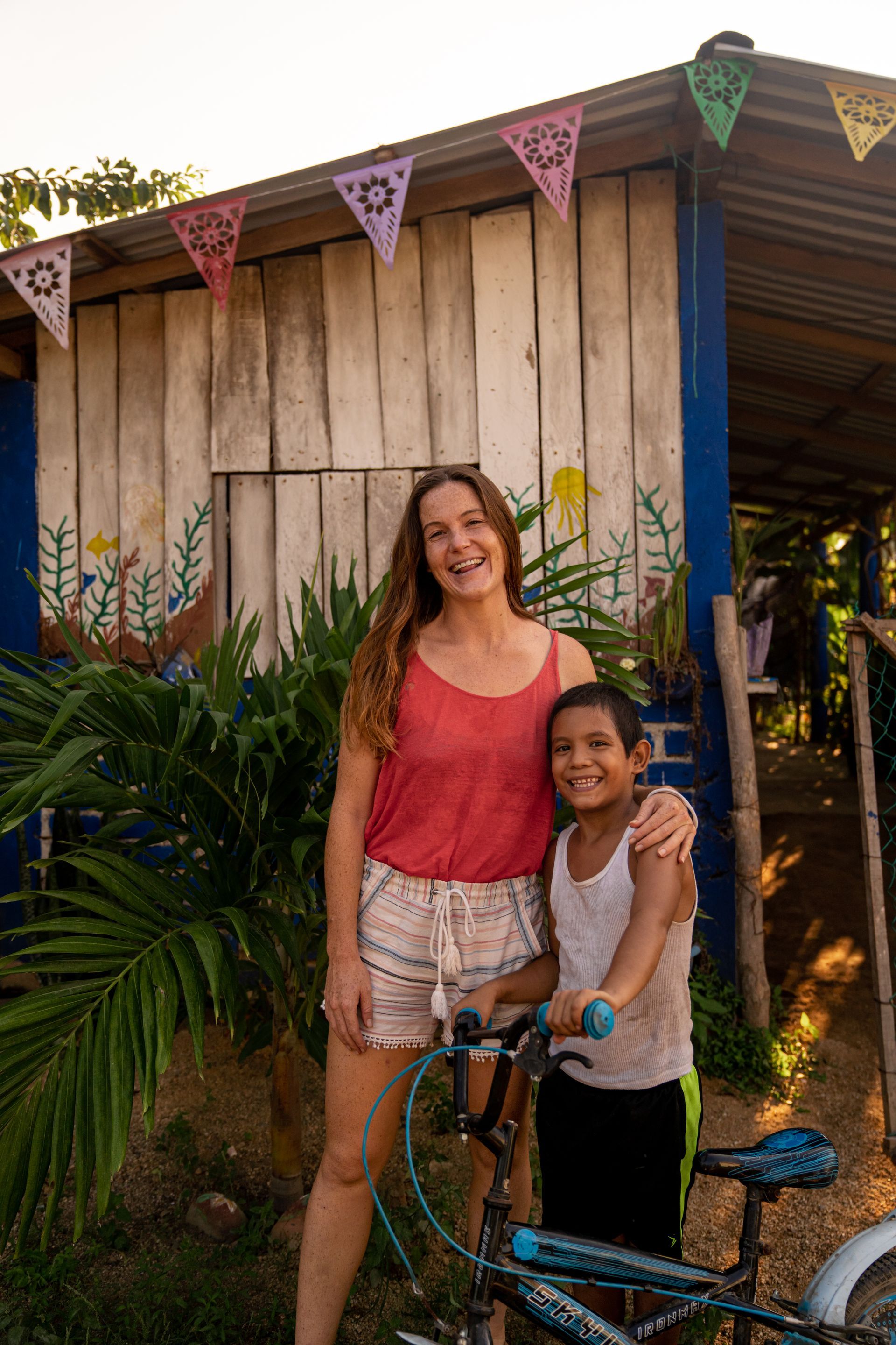 Two people smiling beside a bicycle in front of a rustic wooden building with colorful bunting.