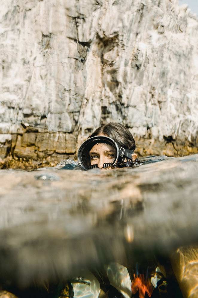 Person snorkeling in clear water near a rocky cliff, with face partly above the surface