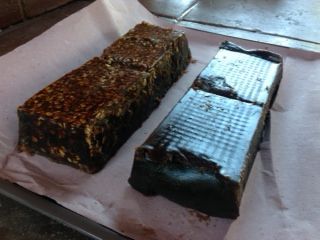 Two rectangular food loaves on parchment, one dark and one glossy black, on a tray.