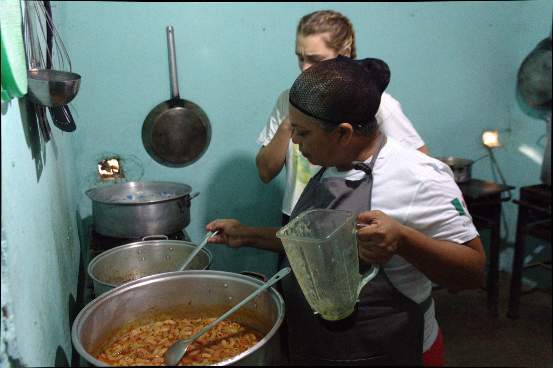 Two people preparing food in a kitchen, stirring a large pot on a stove.