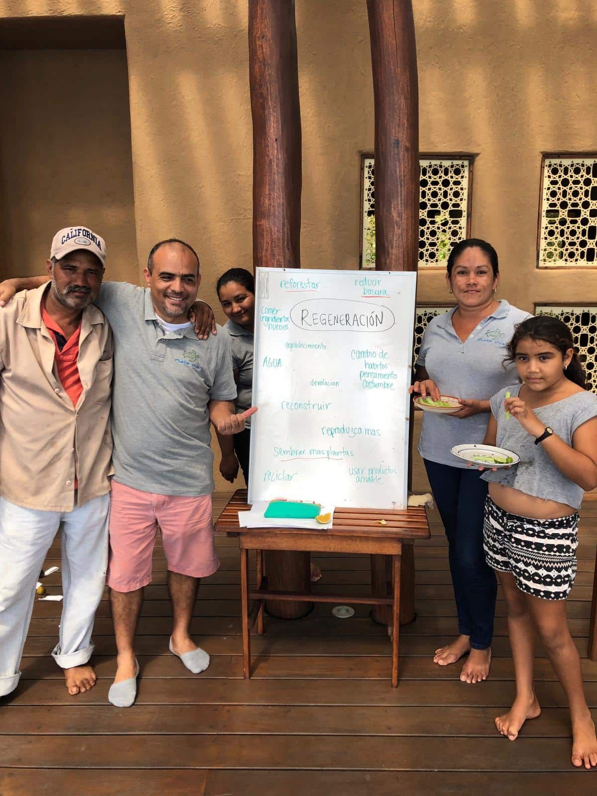 Group posing indoors beside a whiteboard on a wooden deck, with food and drinks in hand.