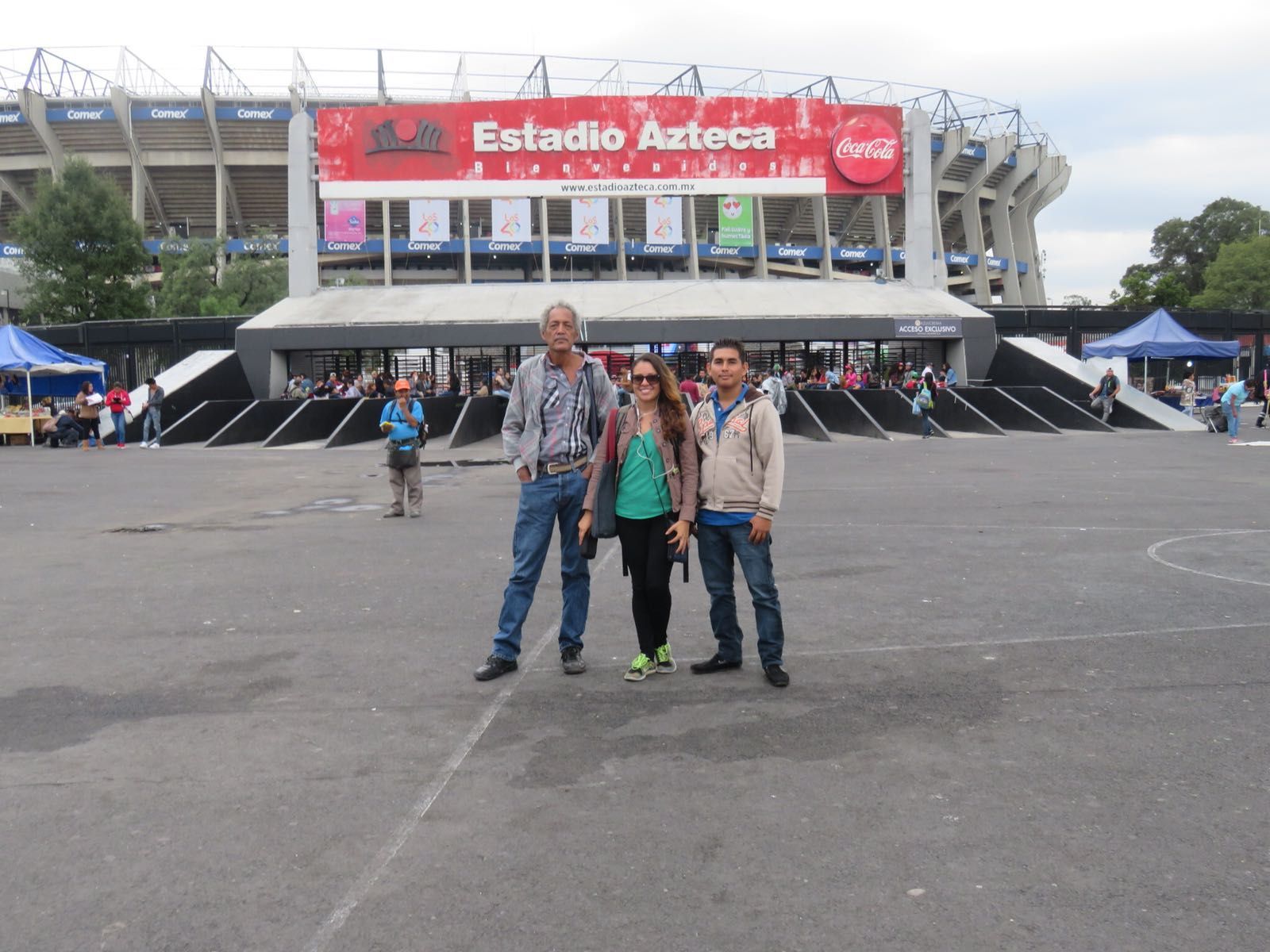 Three people standing in front of Estadio Azteca entrance with a red banner.