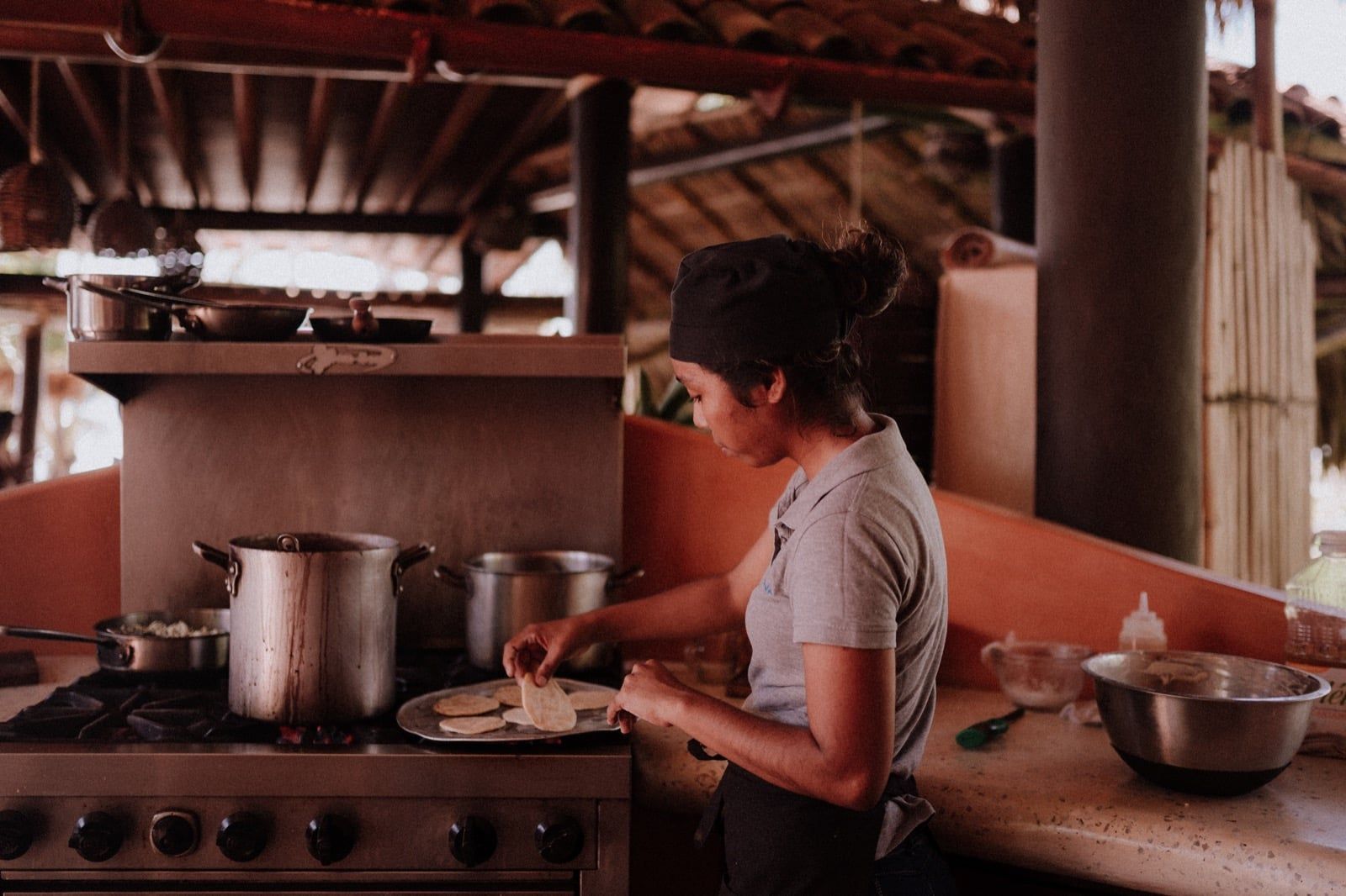 Person cooking at a stove in a rustic kitchen, with pots on the burners and bowls on the counter.