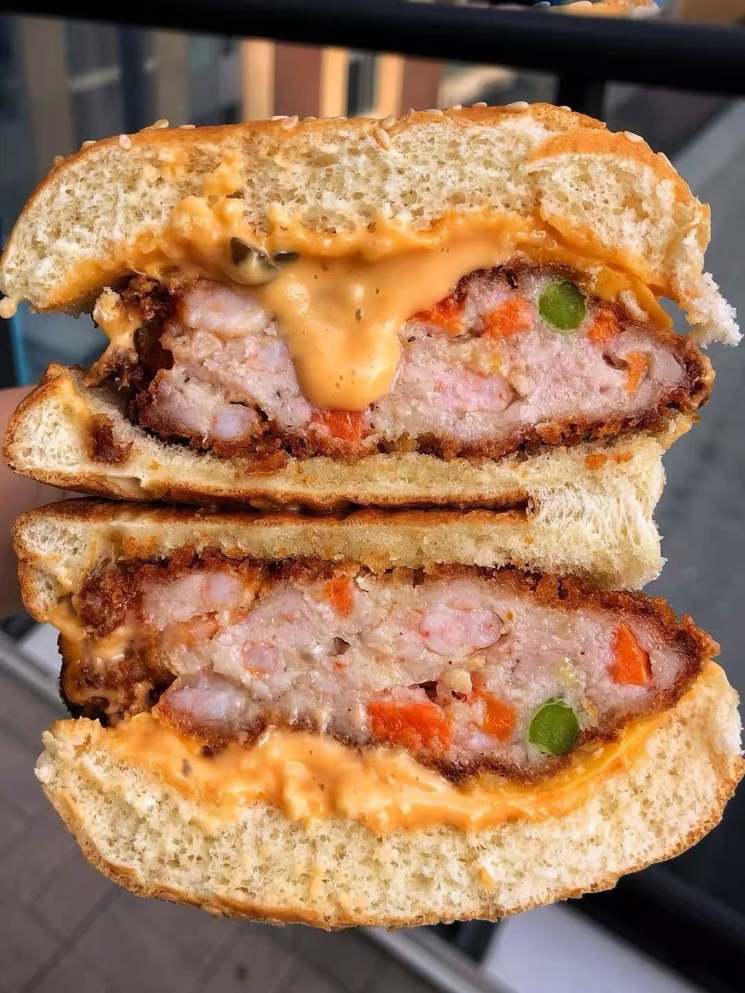 Cross-section of a cheeseburger with melted orange sauce and thick beef patty on a bun