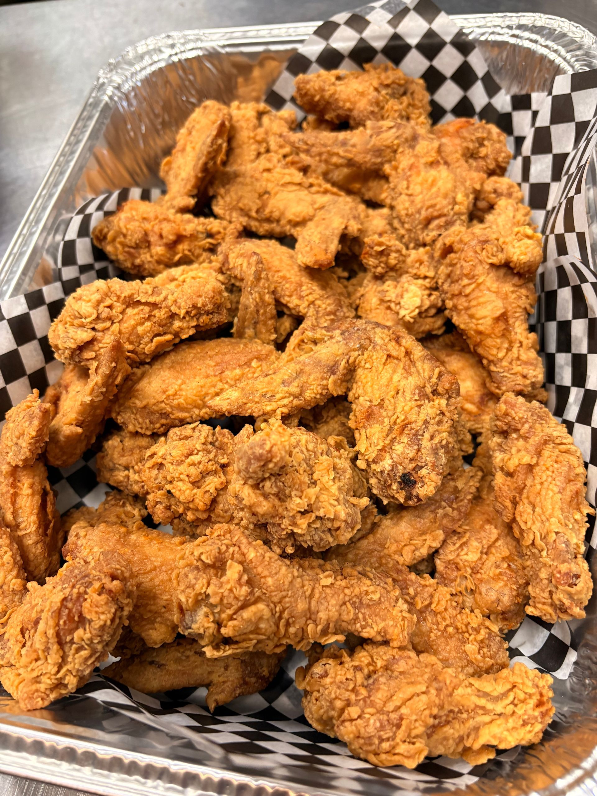 Tray of crispy fried chicken wings in a foil container with checkered liner