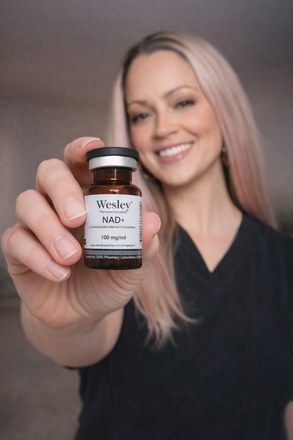 Woman holding out a small black bottle labeled “Wesley” and smiling against a blurred gray background