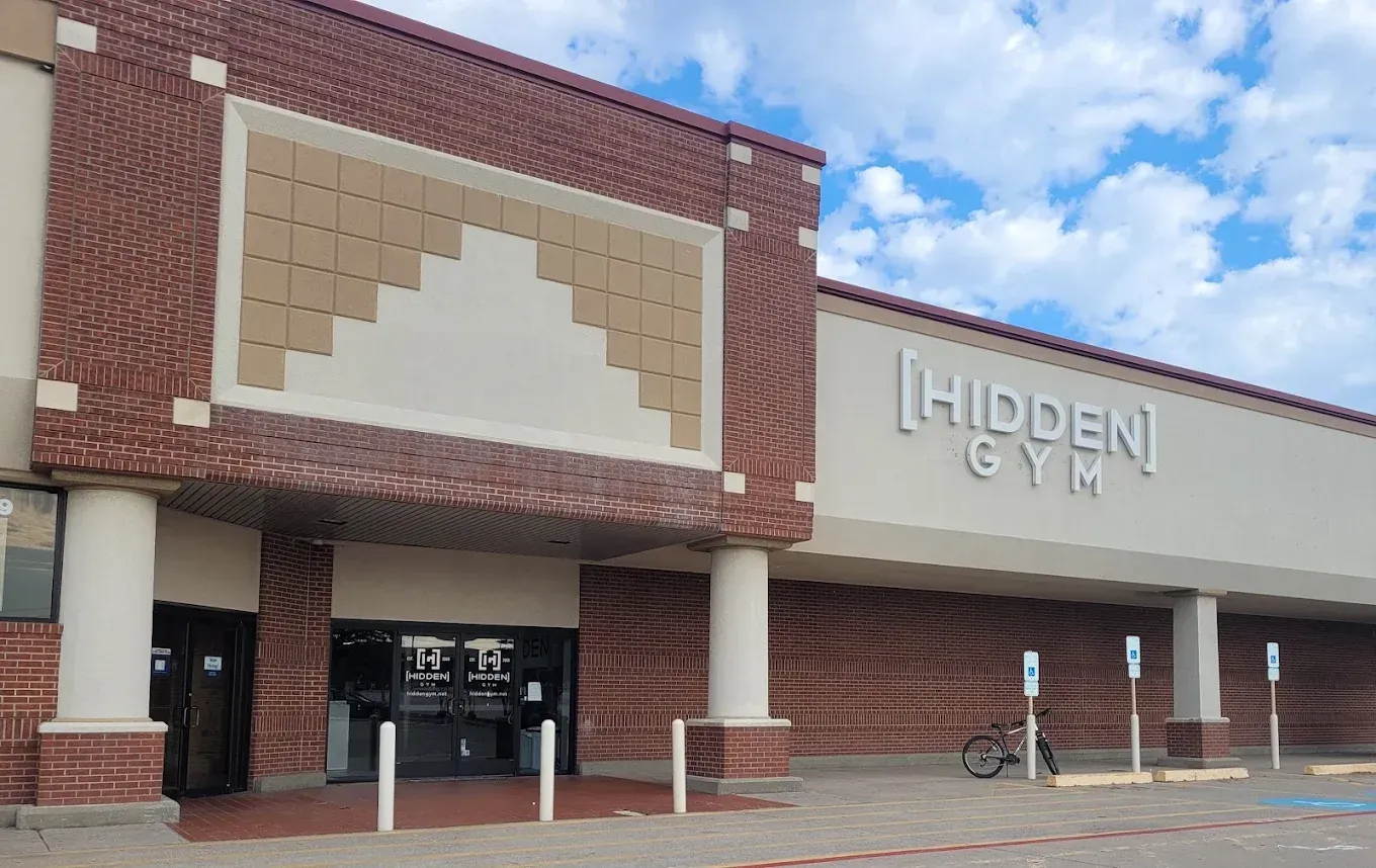 Front entrance of Hidden Gym storefront with brick facade and beige sign under a blue sky