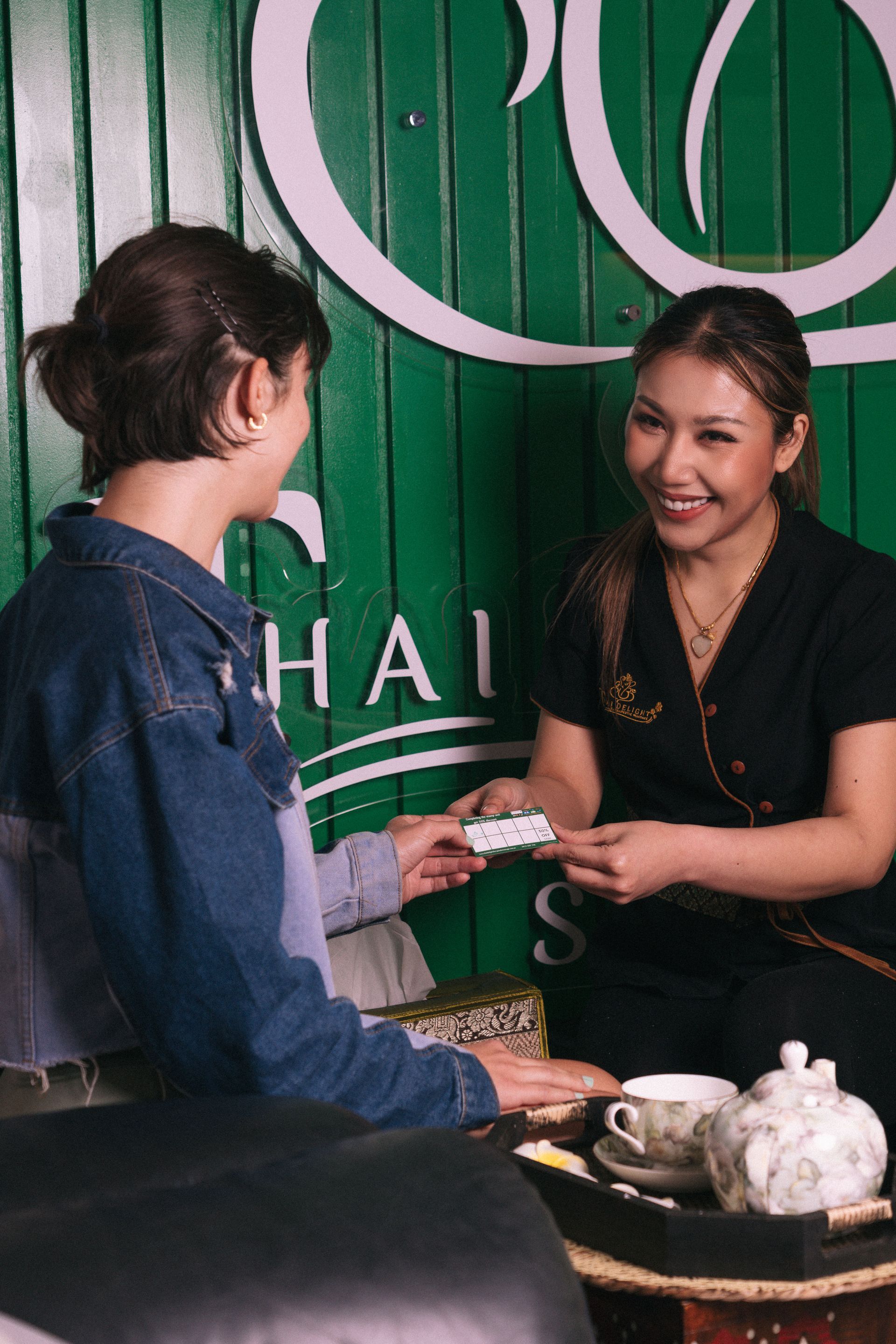 Woman receiving a royalty card from Thai Delight Therapeutic Massage spa employee