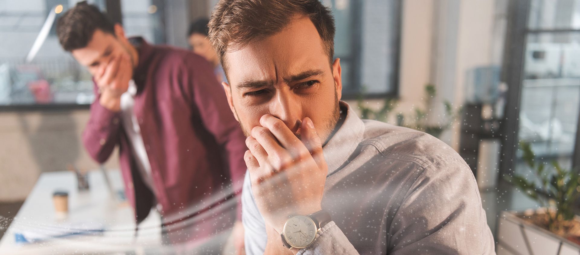 Three men in an office covering their noses, showing expressions of disgust.