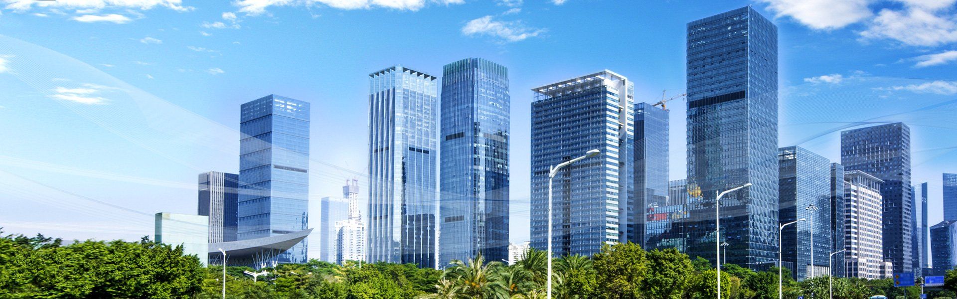 Skyscrapers in a city with a clear blue sky. Green trees at the base of the buildings.