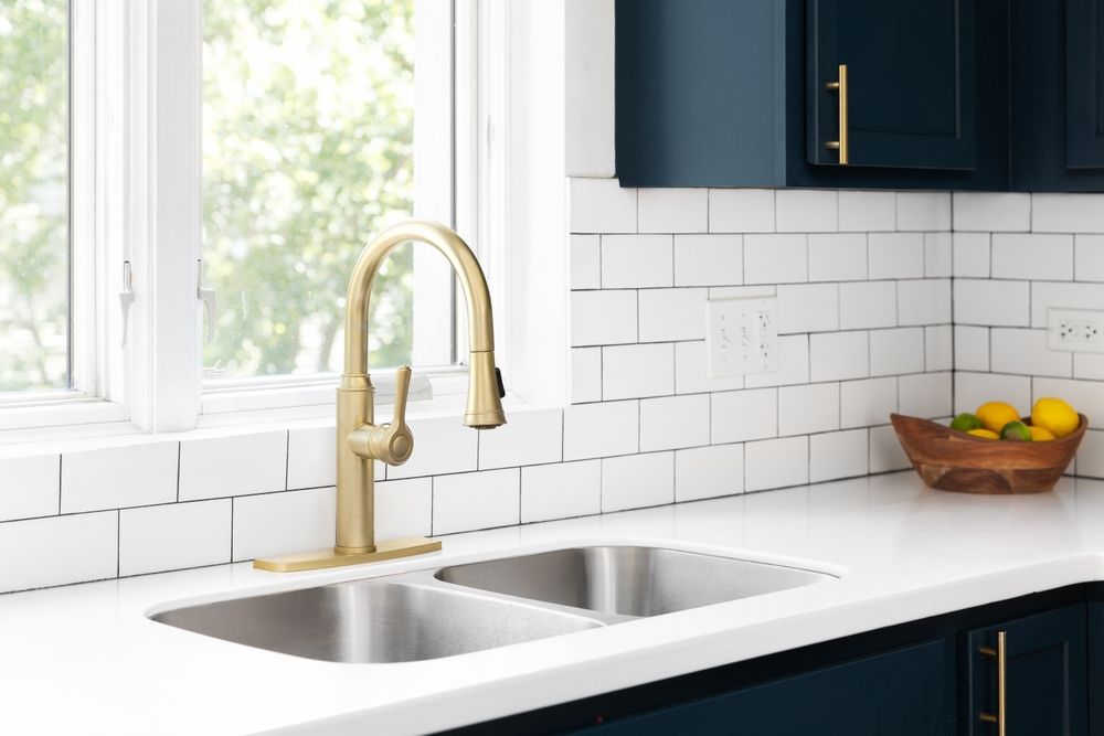 A kitchen sink with a gold faucet and a bowl of lemons on the counter.