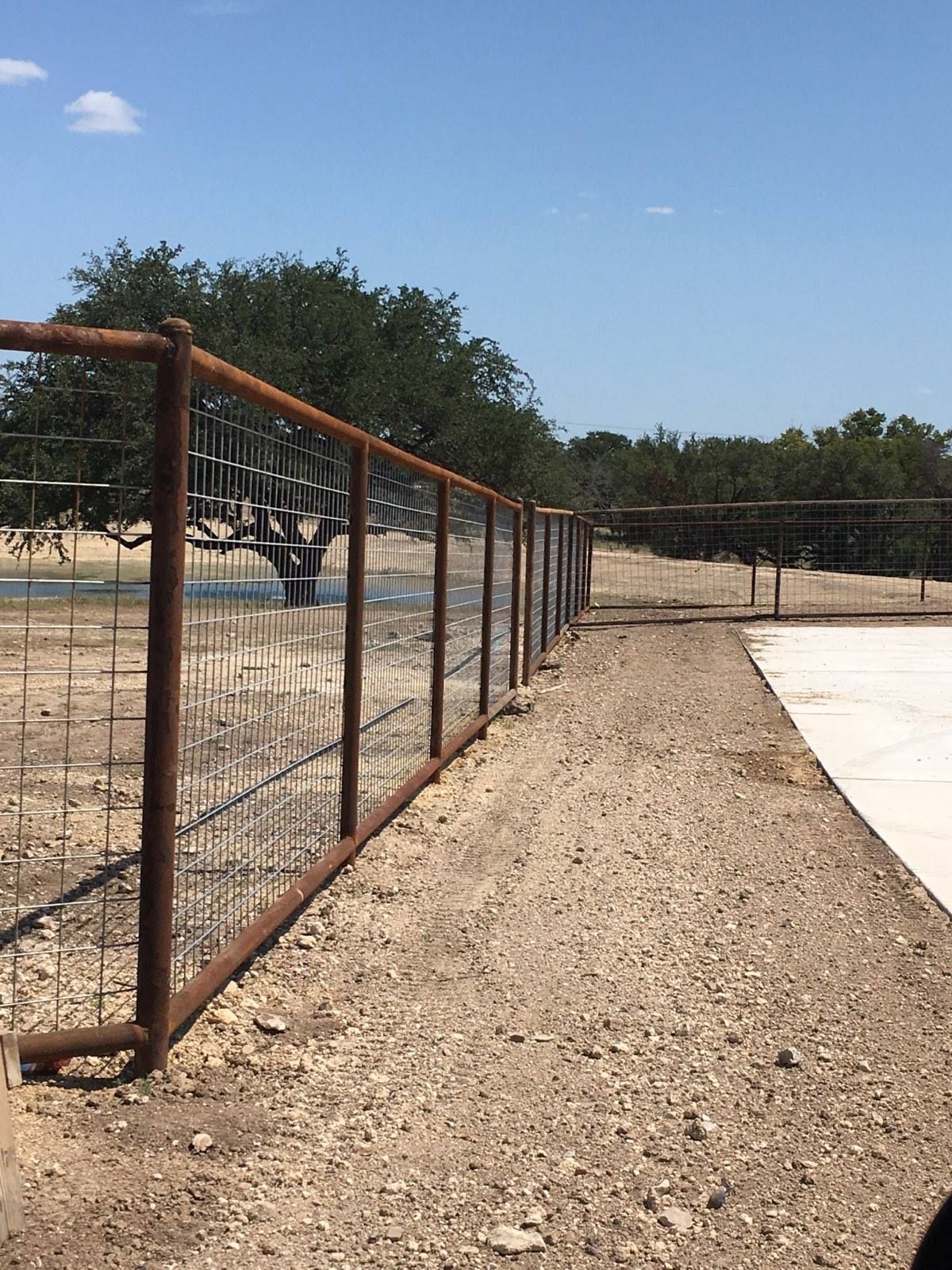 Rusty fence lining a gravel path beside a concrete area under a clear blue sky