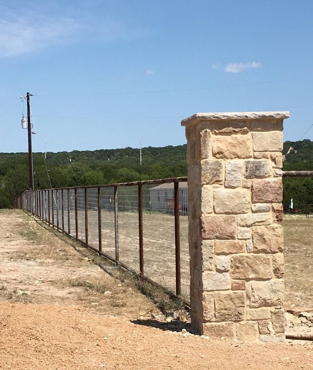 Stone fence and gatepost along a dirt road under a blue sky.