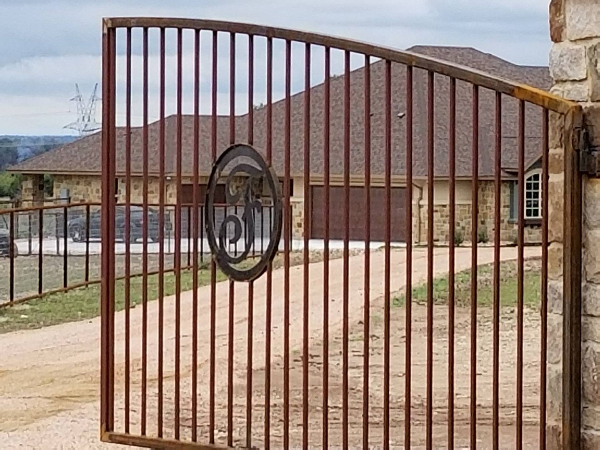Brown metal gate with circular emblem in front of a building and driveway