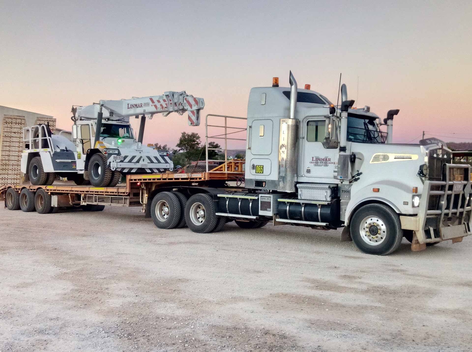 A Semi Truck is Driving Down a Desert Road at Sunset — Linmar Cranes & Haulage in Kalkadoon, QLD
