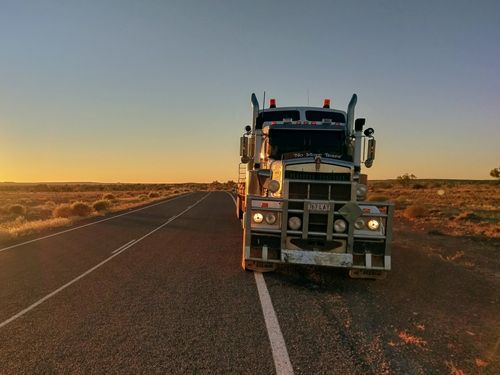 A Semi Truck Is Driving Down a Desert Road at Sunset — Linmar Cranes & Haulage in Karumba, QLD