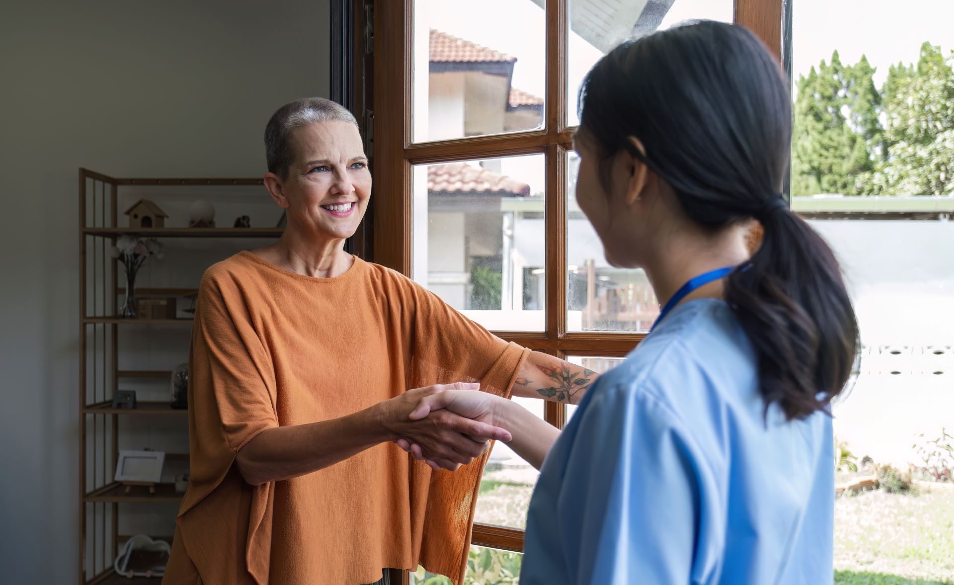 Healthcare worker shaking hands with an older woman in a bright home doorway