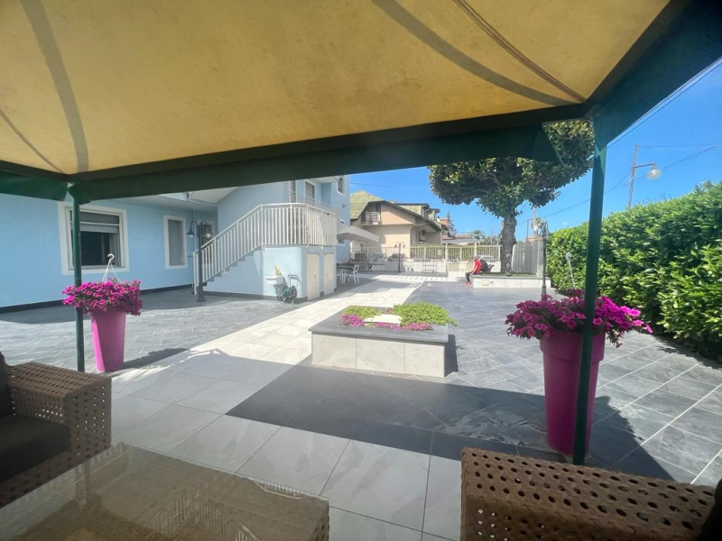 Patio con casa blu, posti a sedere e vasi di fiori rosa.