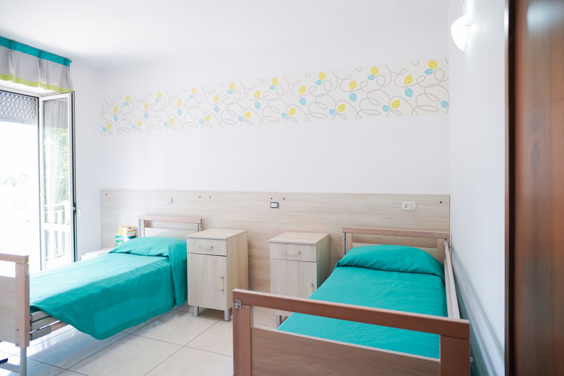 Due letti in una stanza luminosa, con biancheria da letto turchese, comodini e pareti decorate.
