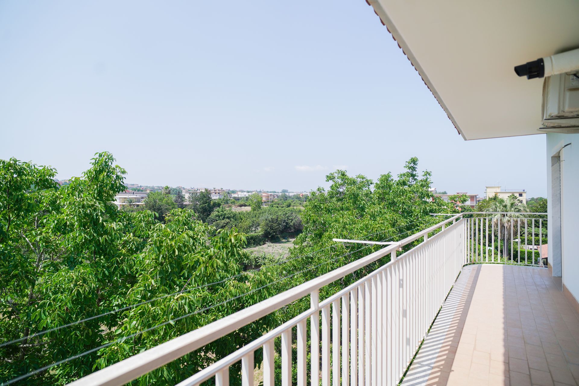 Balcone con vista su rigogliosi alberi verdi e edifici in lontananza nelle giornate di sole.