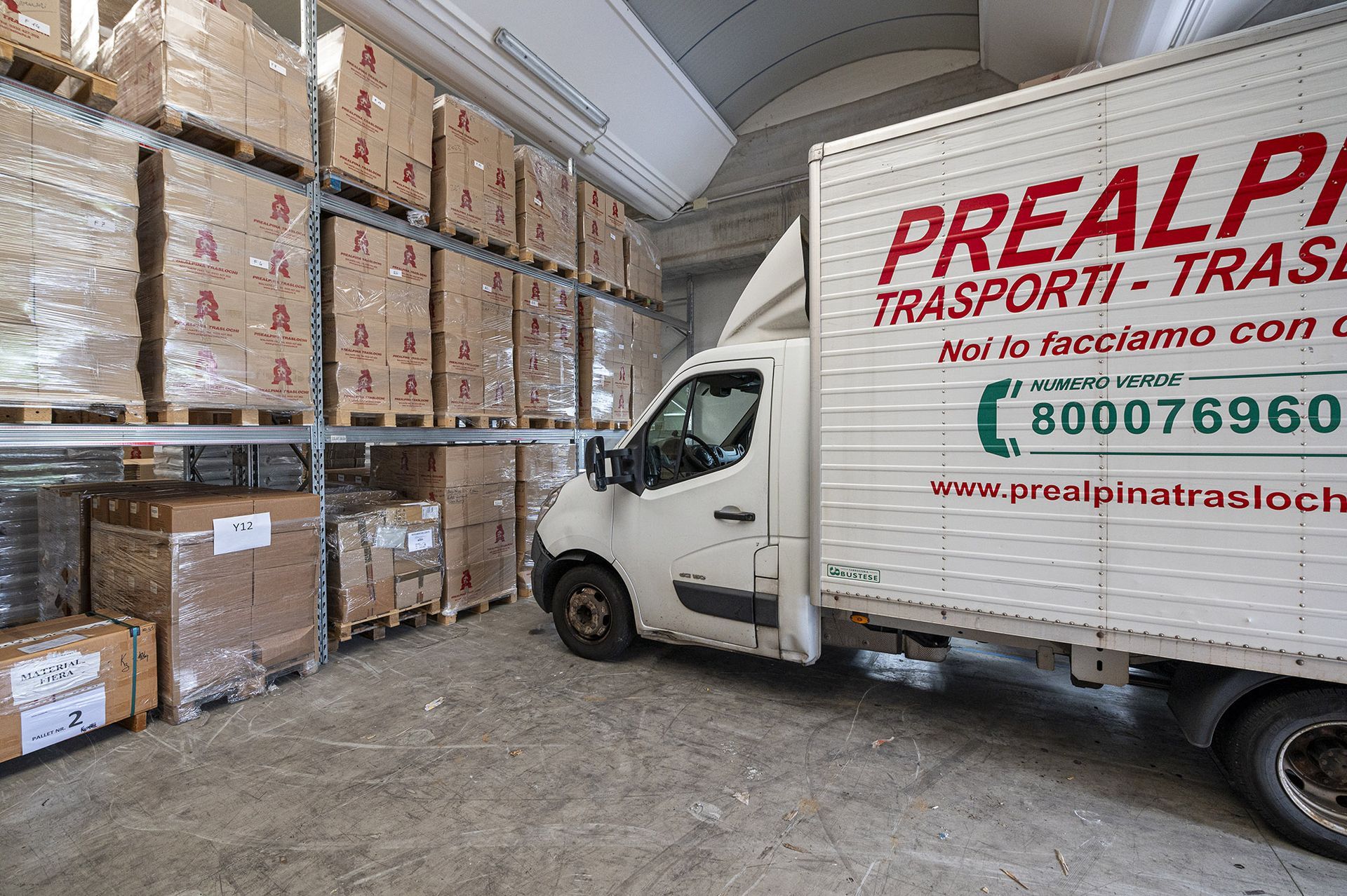 Camion parcheggiato in un magazzino accanto a scaffali pieni di scatole.