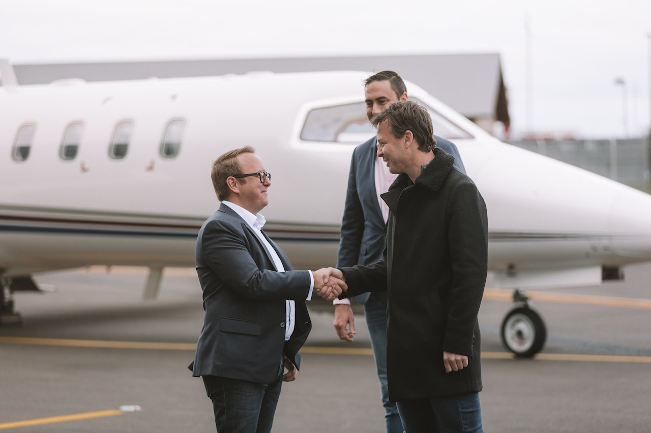 Three men are shaking hands in front of a private jet.