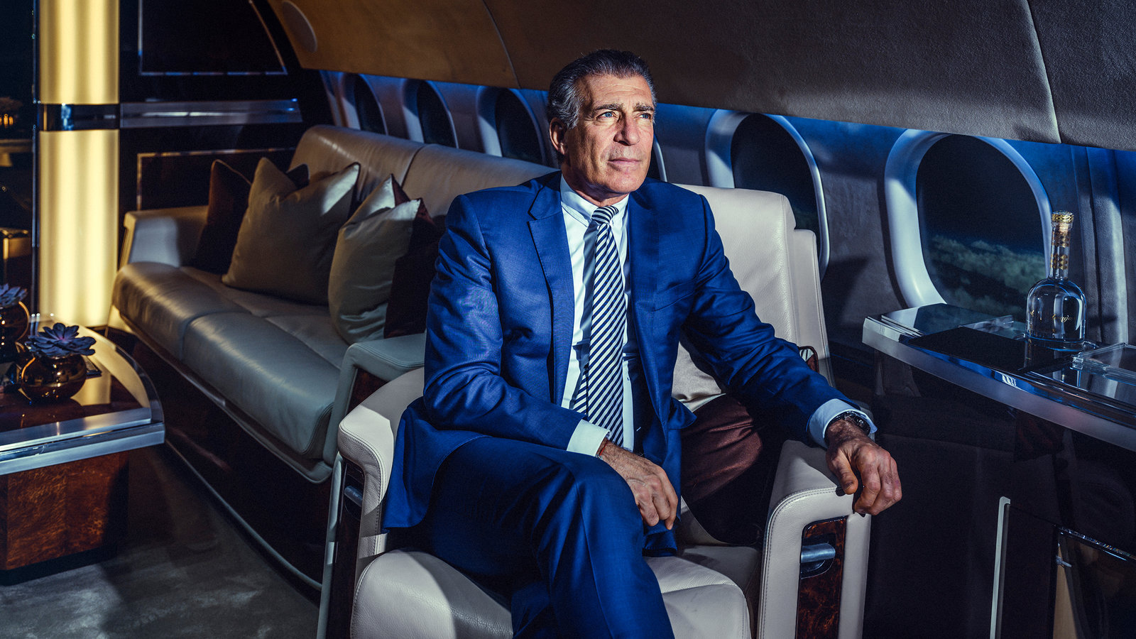 A man in a suit and tie is sitting in a chair on a private jet.