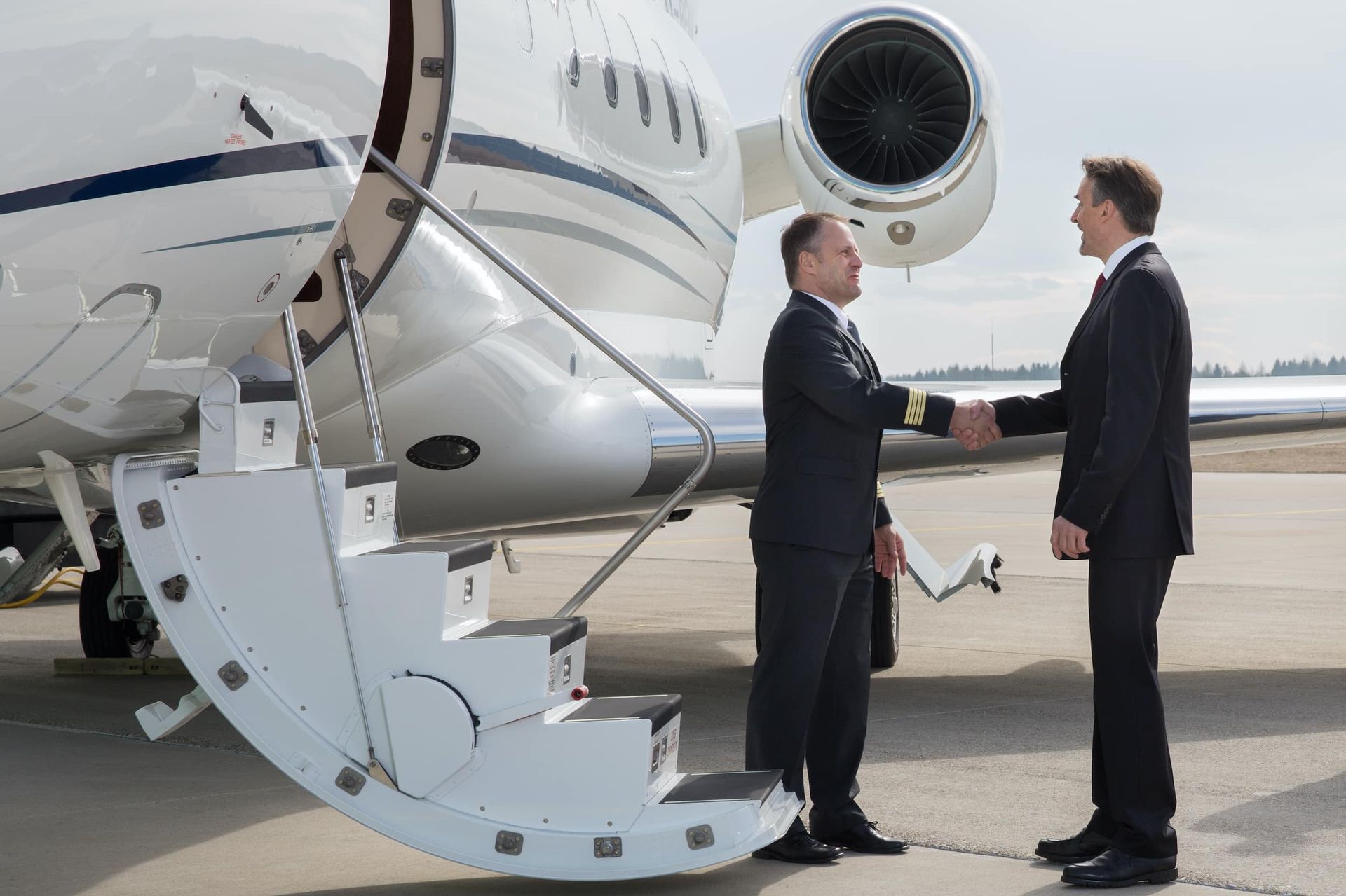 Two men are shaking hands in front of a private jet.