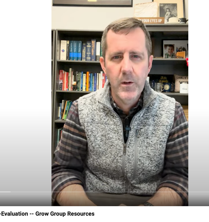 A man in a vest is sitting in front of a bookshelf