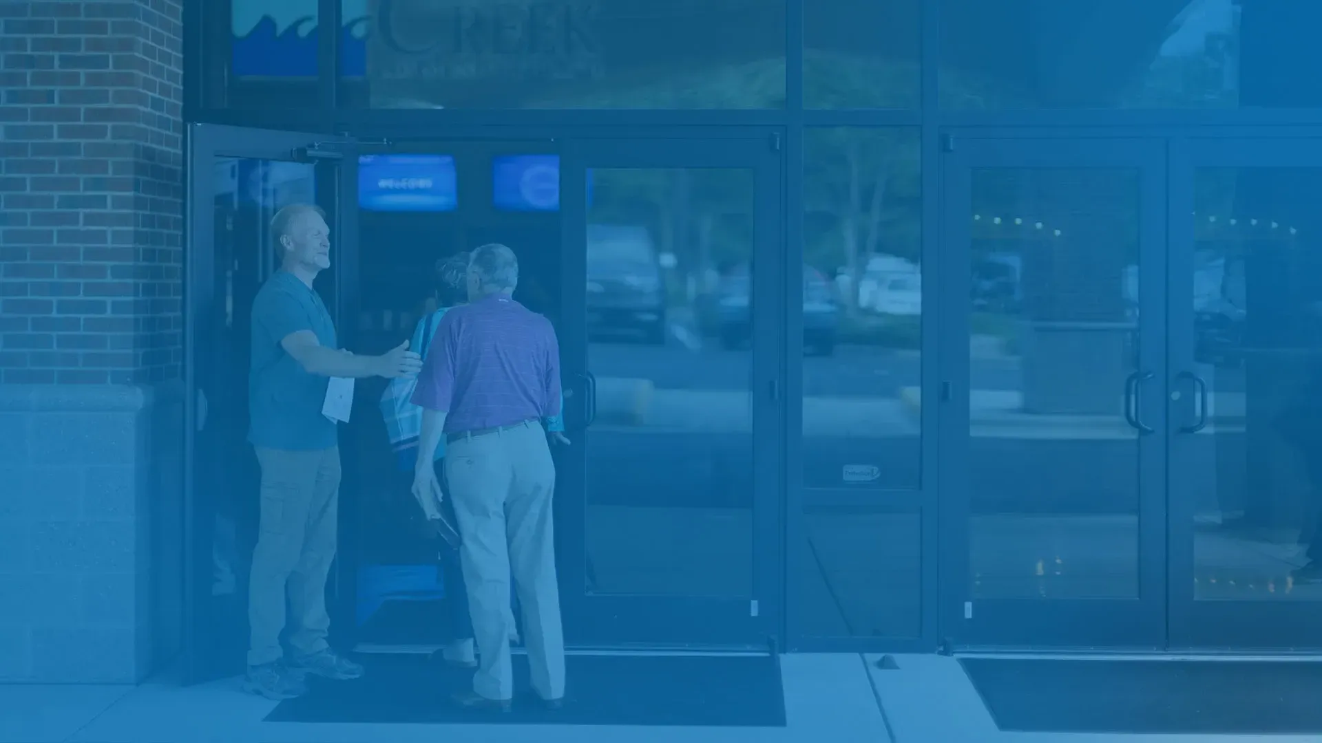 A man is greeting a family entering a building.