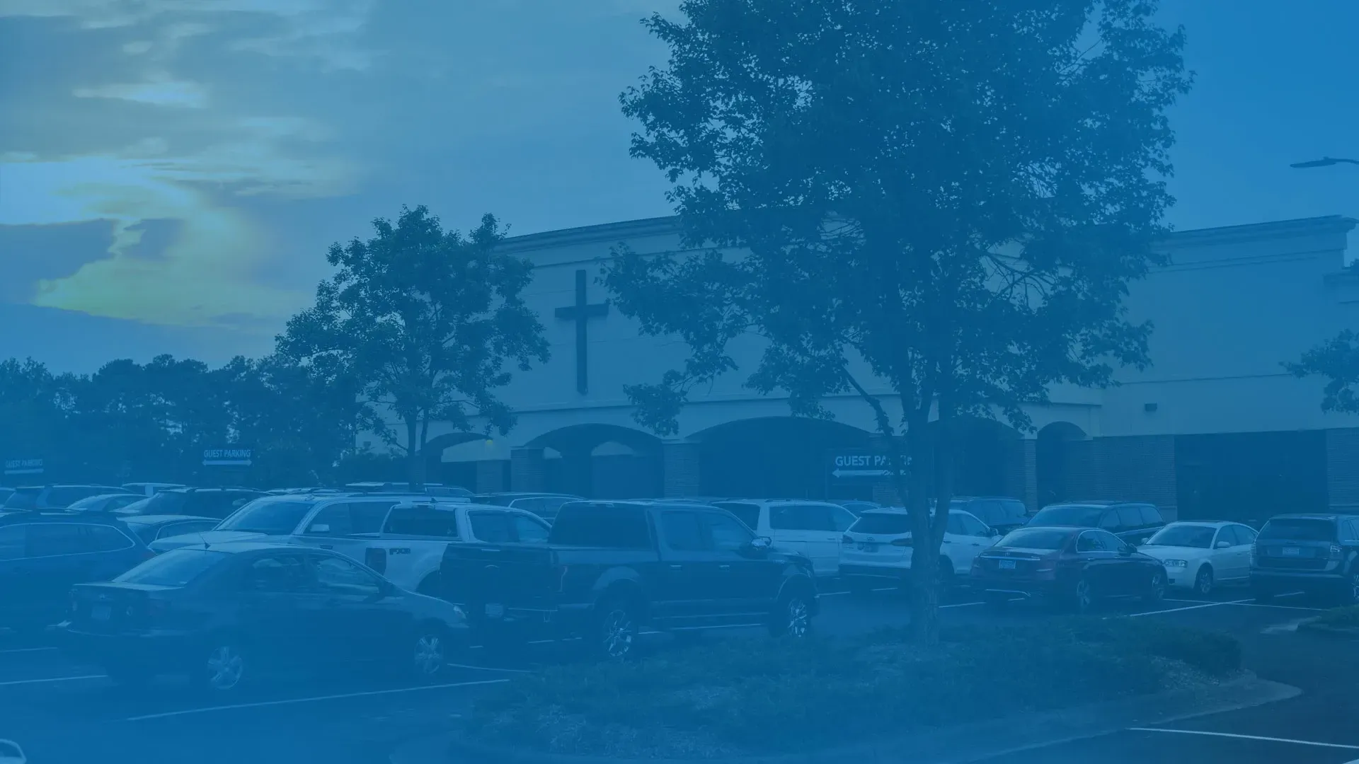 A lot of cars are parked in front of a building with a cross on it.