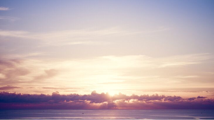 The sun is shining through the clouds over the ocean.