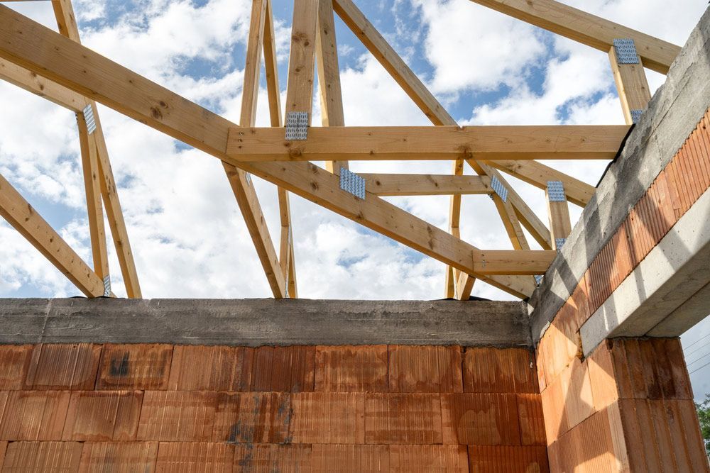 Brick House With Wooden Roof Truss, Support Beams And Ceilings Against Blue Sky — Trussted Frames & Trusses in Warners Bay, NSW