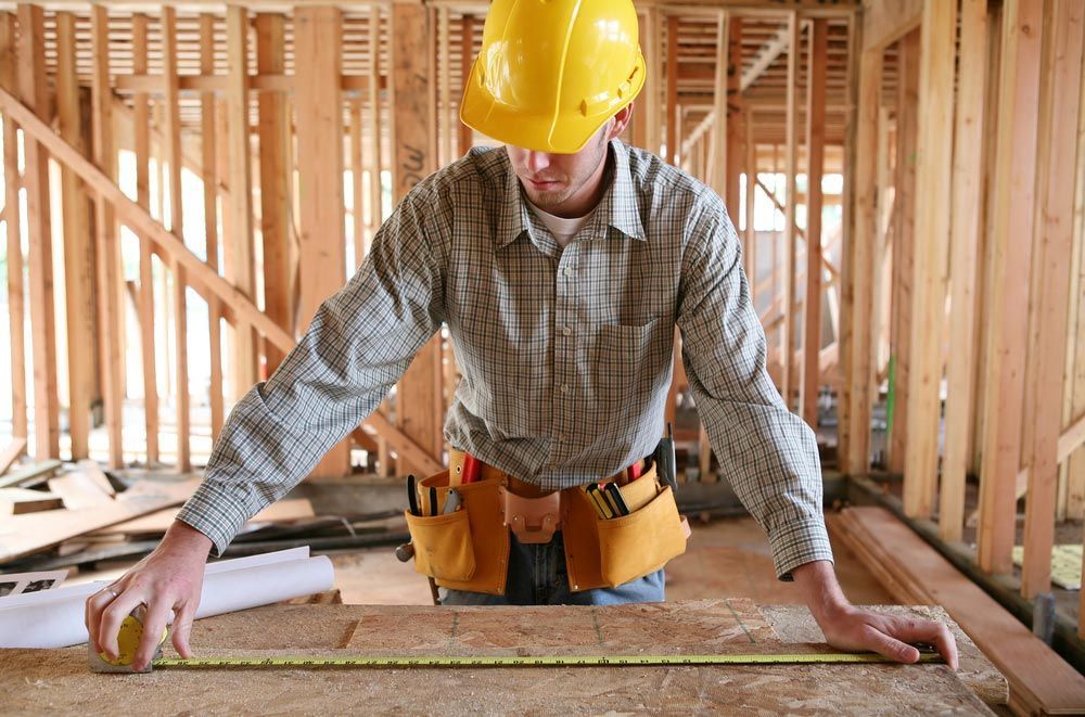 A Man Working Building A Timber Home And Measuring Some Wood — Trussted Frames & Trusses in Warners Bay, NSW