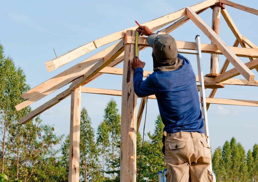 A Man Is Standing On A Ladder Working On A Wooden Home Structure — Trussted Frames & Trusses in Armidale, NSW