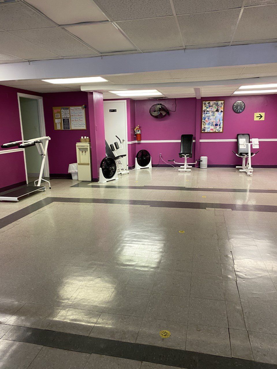 Empty gym room with purple walls, exercise equipment, and a large mirrored wall.