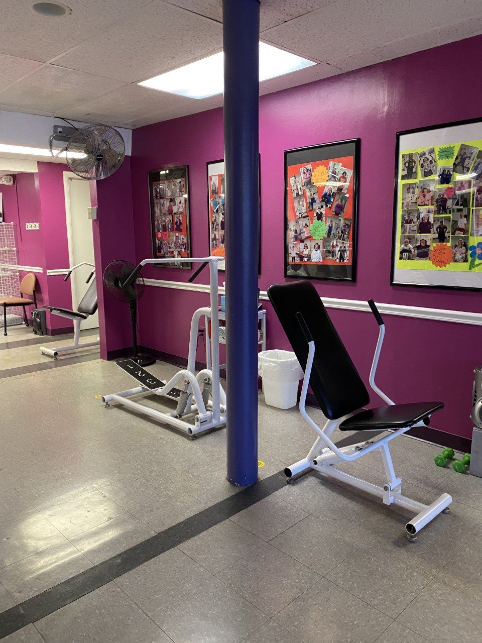 Small gym with purple walls, mirrors, and exercise machines, including a black incline bench in the foreground.
