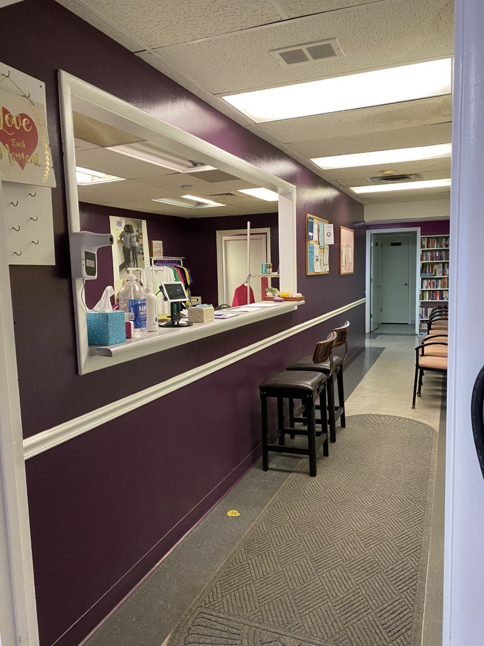 Salon waiting area with purple walls, reception window, stools, and a doorway down the hall