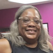Smiling person with glasses and long gray hair in a room with magenta walls