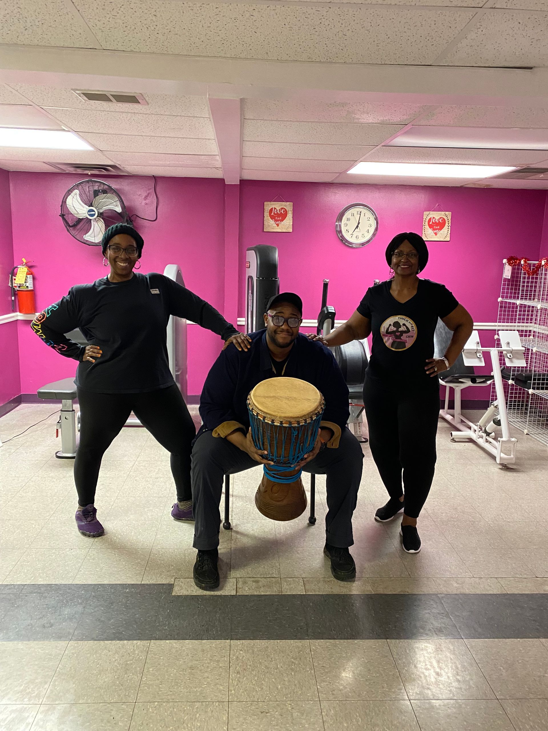 Three people posing with a drum in a bright pink music room