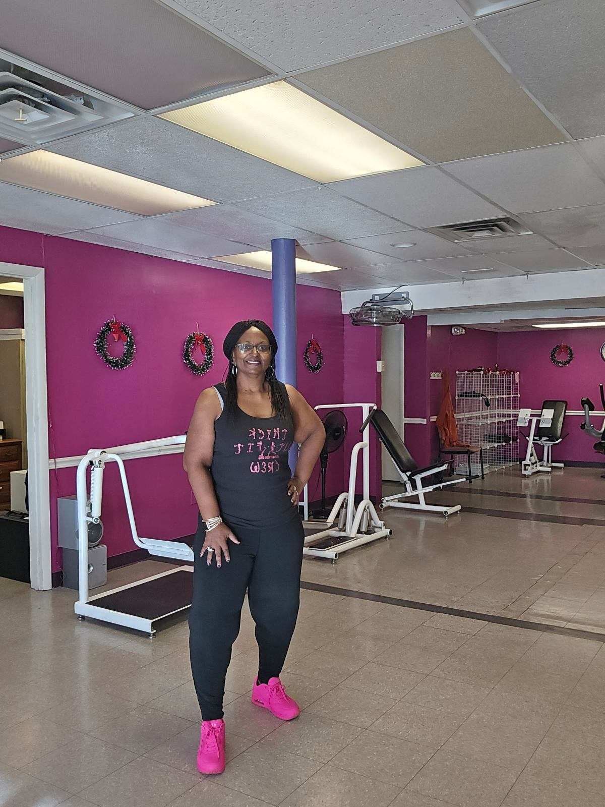 Woman standing in a gym with pink walls, exercise equipment, and bright pink shoes