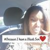 Woman in a car holding a black sign with white text and a red heart.