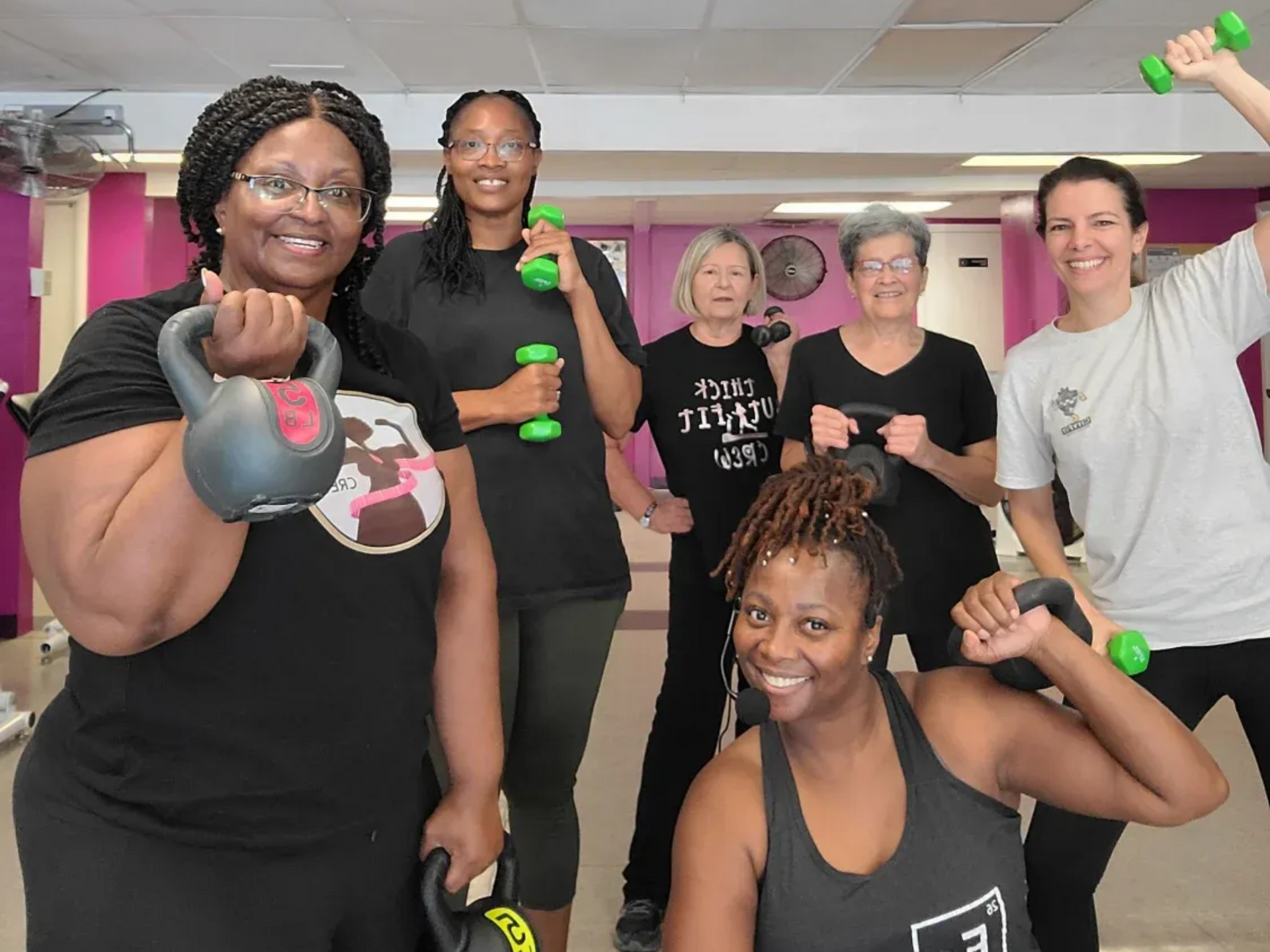 Group of people smiling and posing with green dumbbells in a gym studio