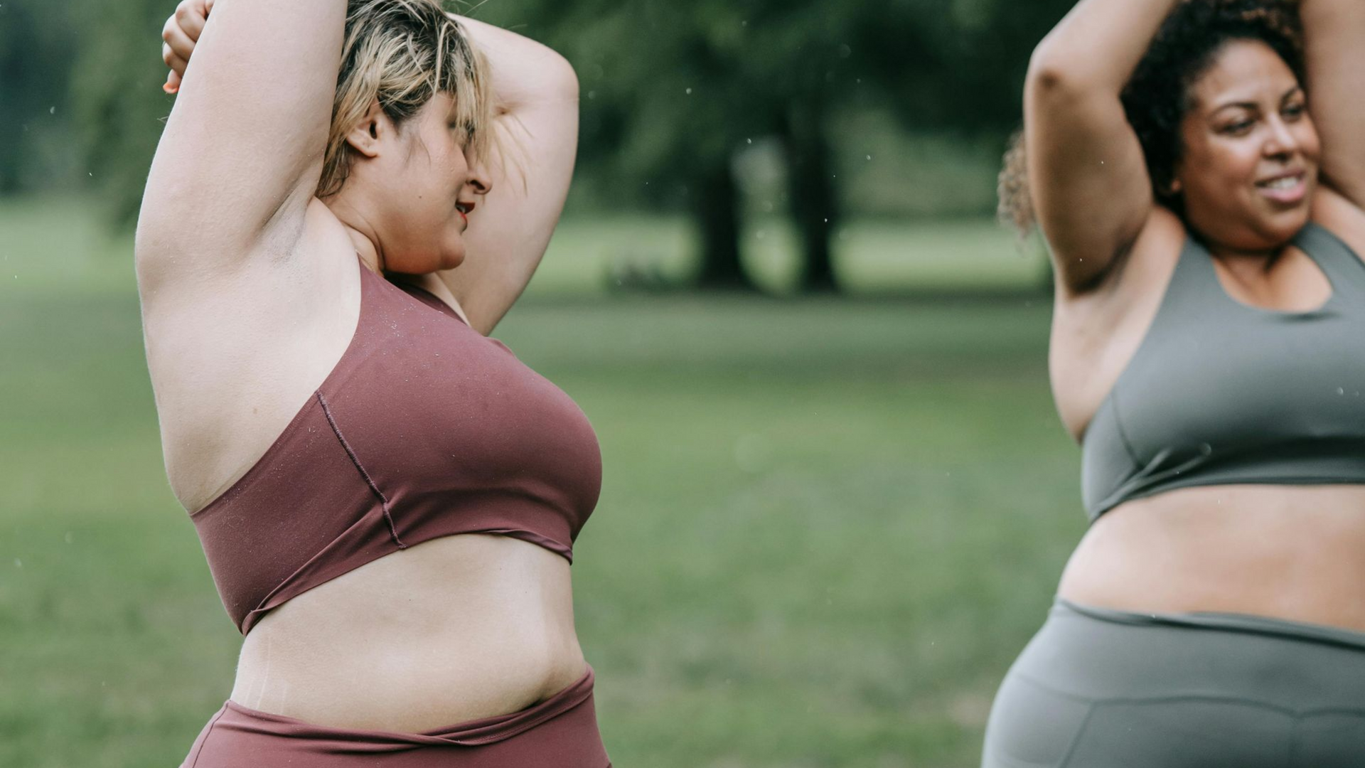 Two people in workout clothes stretching outdoors on a grassy field