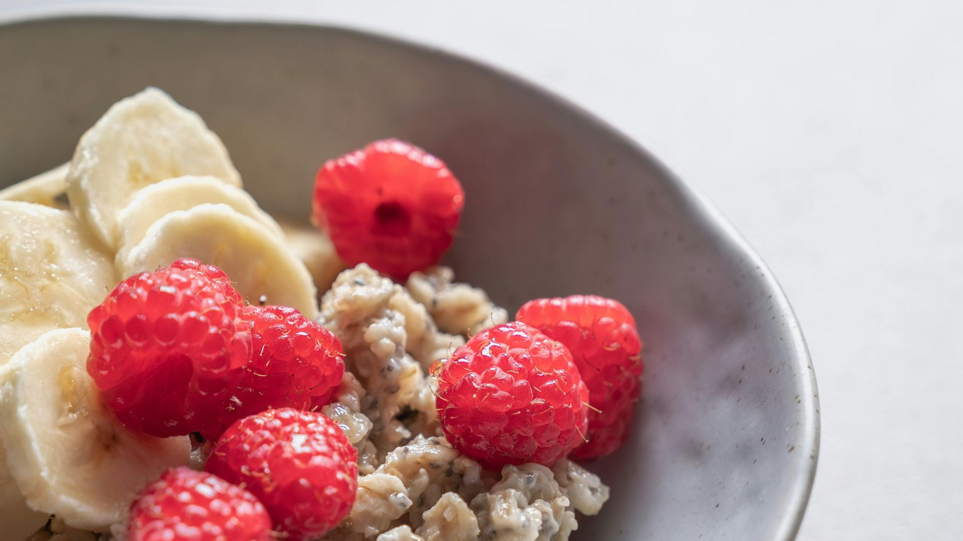Bowl of oatmeal topped with raspberries and banana slices