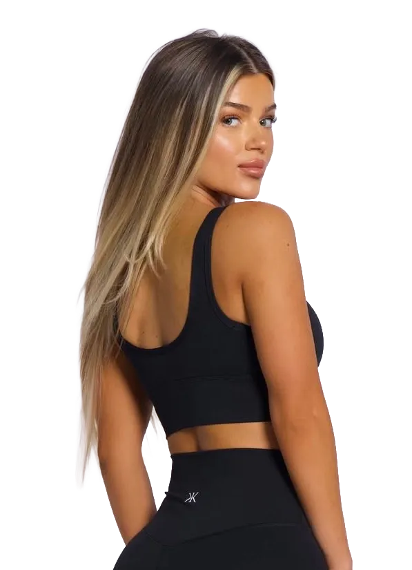 Woman in black athletic wear posing against a white background, showing a back view.